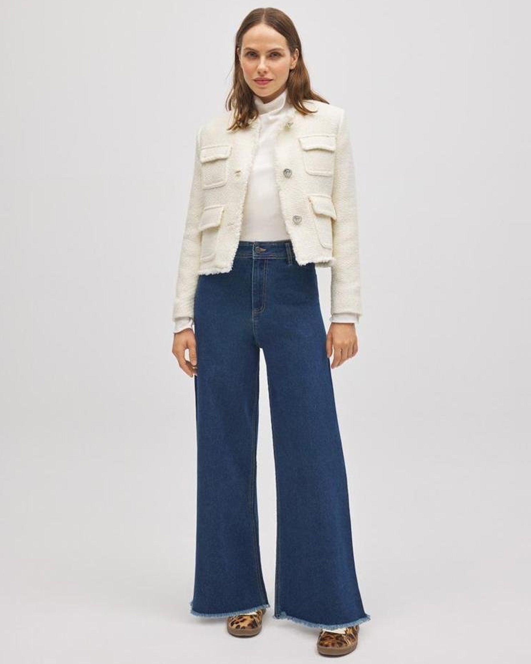 Woman wearing a white jacket and blue wide jeans on a plain background