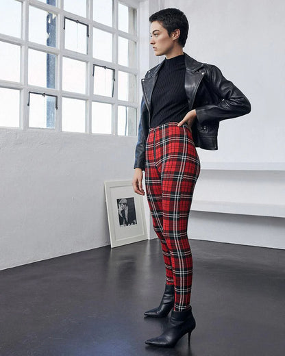 Person wearing a black leather jacket, black top, and red plaid pants in a modern room.