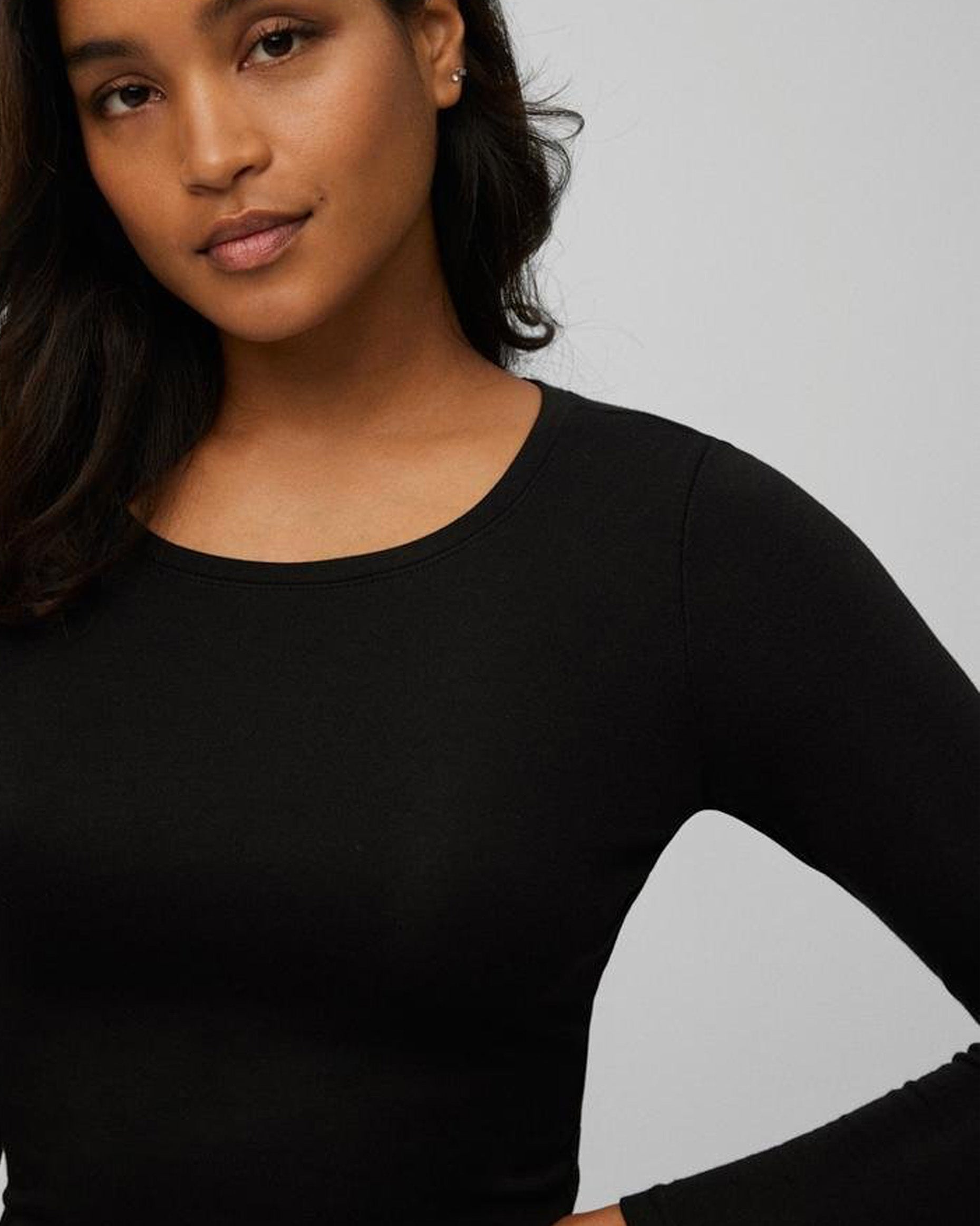 Woman wearing a black long-sleeve top against a gray background