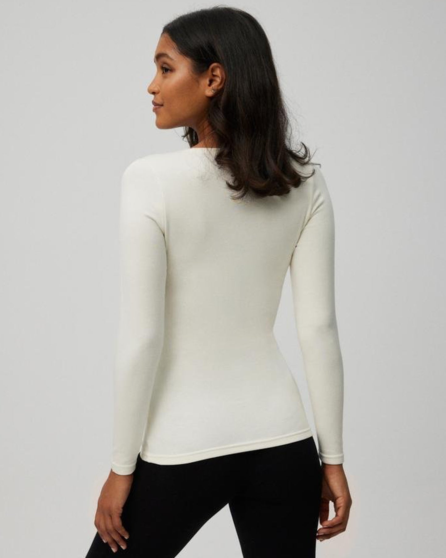 Woman wearing a white long-sleeve top against a gray background, back view