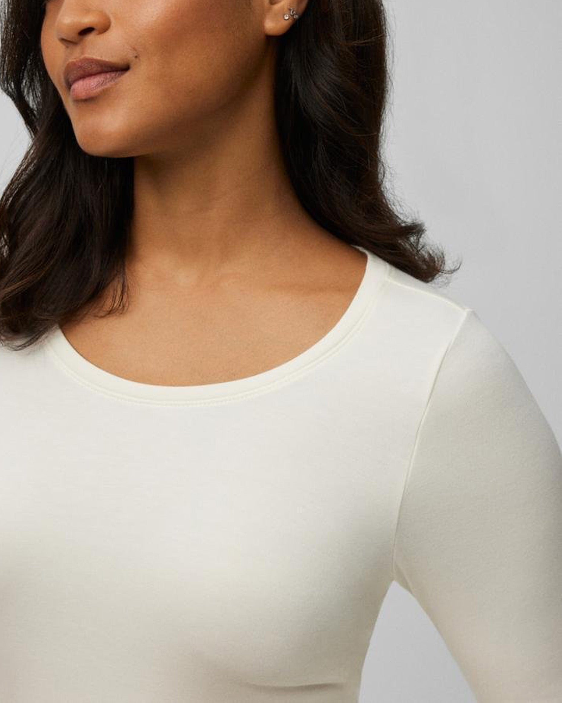 Close-up of a person wearing a white long-sleeve top against a gray background