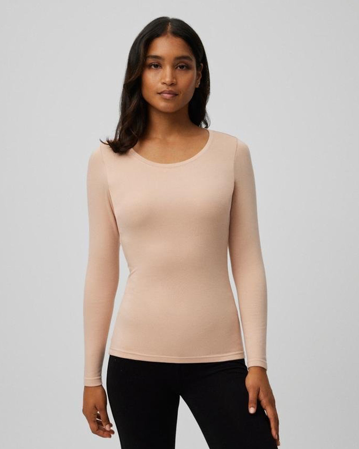 Woman wearing a beige/nude long-sleeve crew neck top against a plain background