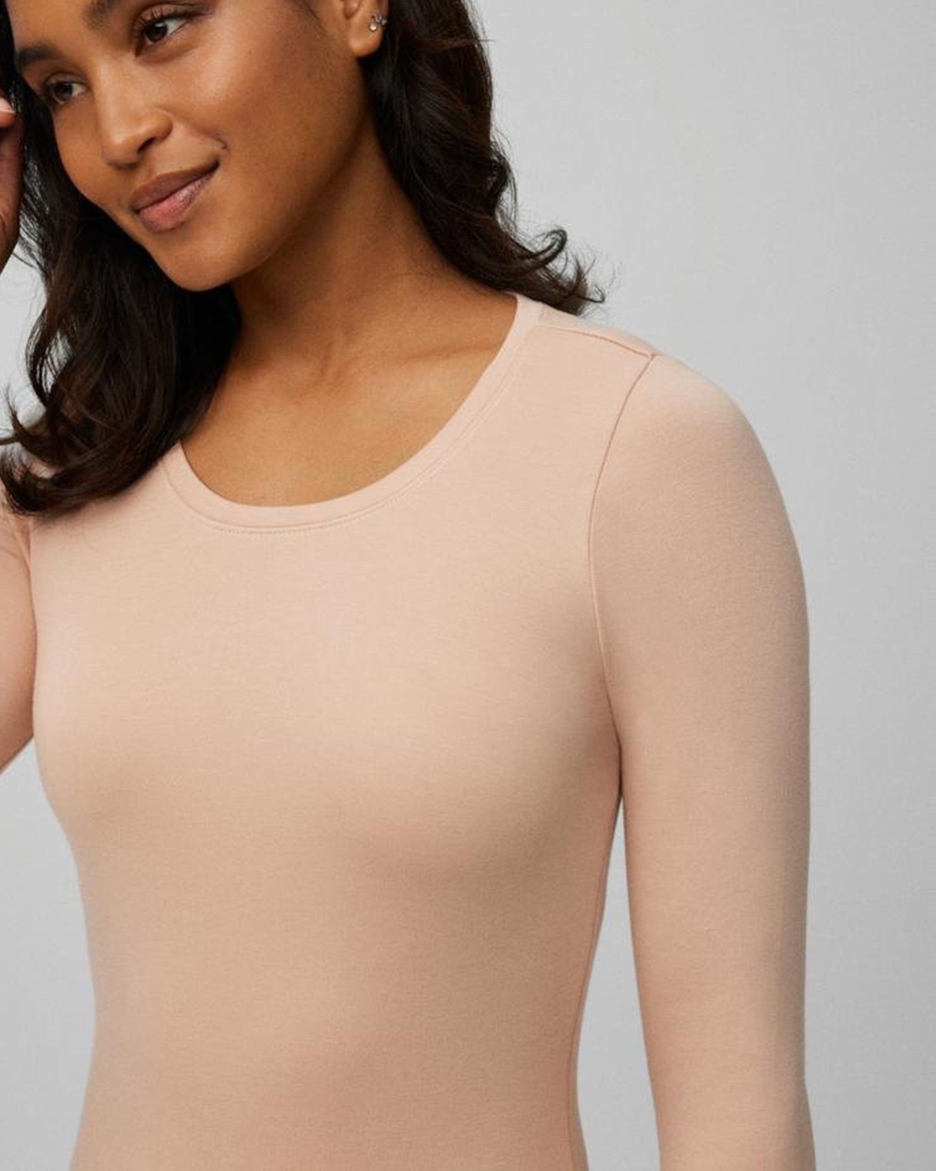 Woman wearing a beige long-sleeve top against a plain background