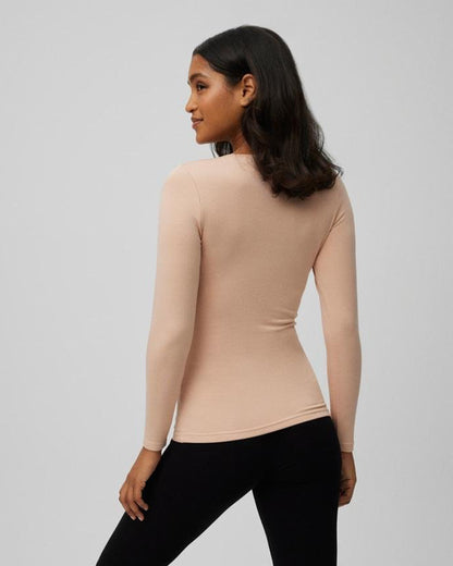 Woman wearing a beige long-sleeve top and black pants on a gray background, back view