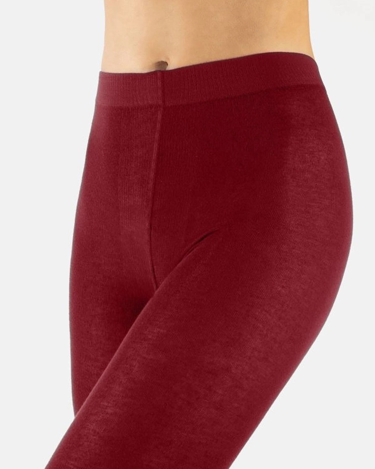 A close-up side view of a person wearing ribbed burgundy leggings against a light gray studio background.