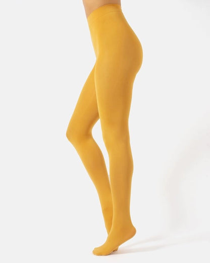 A model's legs wearing solid mustard yellow tights, shown from the waist down in a side profile against a clean white studio background.