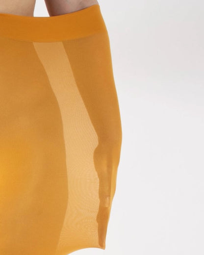 Close-up of an opaque mustard yellow tight worn by a model with their arm inside to demonstrate how stretchy they are