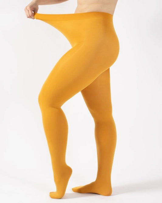 A person wearing solid mustard yellow tights, shown from the waist down, stretching the fabric at the waistband against a clean white background.