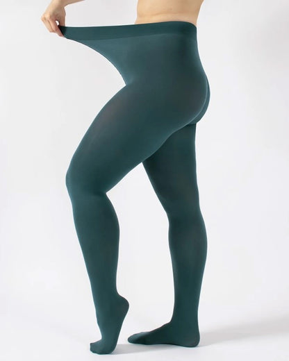A model wearing dark teal green tights, lifting the waistband to show fit and transparency, against a plain white studio background.