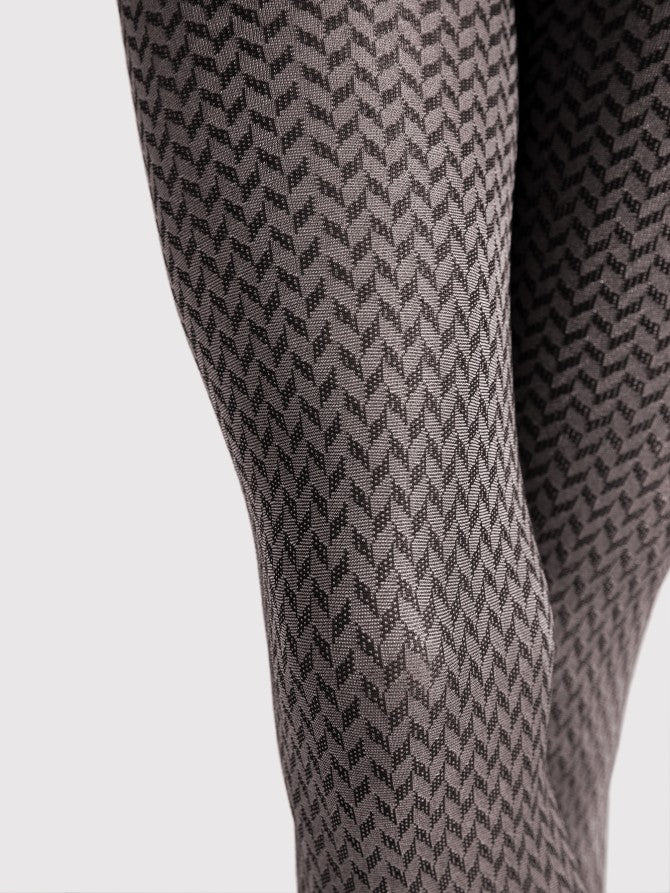 Fiore Cinematic Tights - Close up of a light silver grey glossy fashion tights with an all over black chevron style pattern.