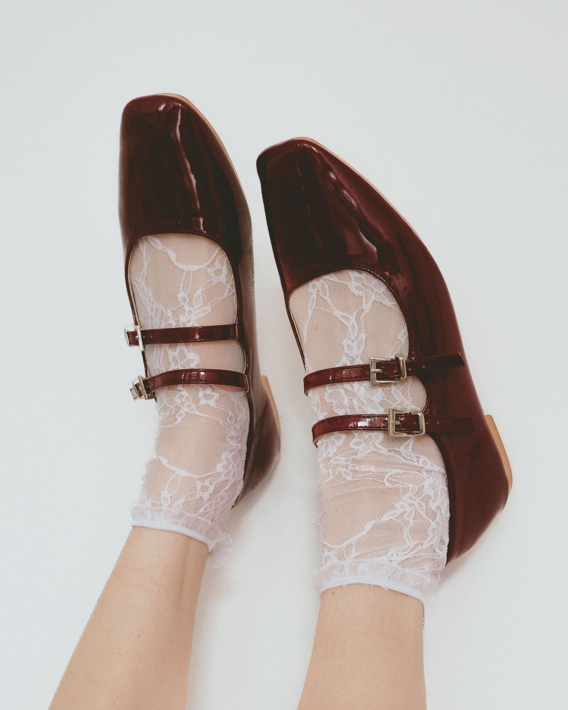 Burgundy shoes with a strap worn with white lace socks on a light background