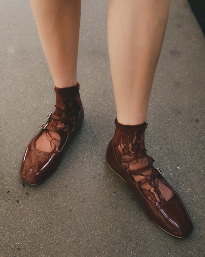 Brown patent leather shoes worn with sheer brown floral lace socks on a concrete surface