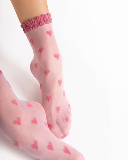 Sheer pink tights with heart patterns worn by a person on a white background