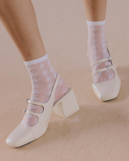 White high-heeled shoes with dogtooth pattern sheer socks on a beige background