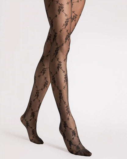 Black floral lace tights worn on legs, shown from the thighs to the feet against a plain light gray studio background.