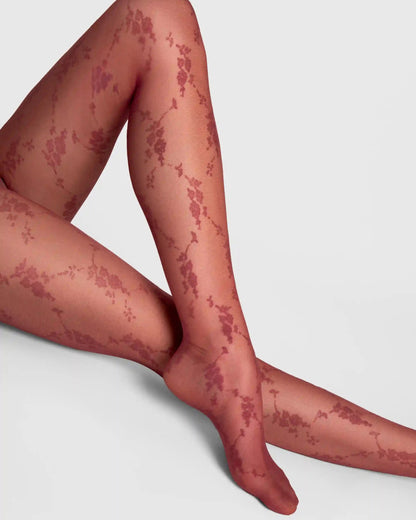 A close-up of a model's legs wearing sheer tights with a dark burgundy red rose floral pattern, set against a plain light gray background.