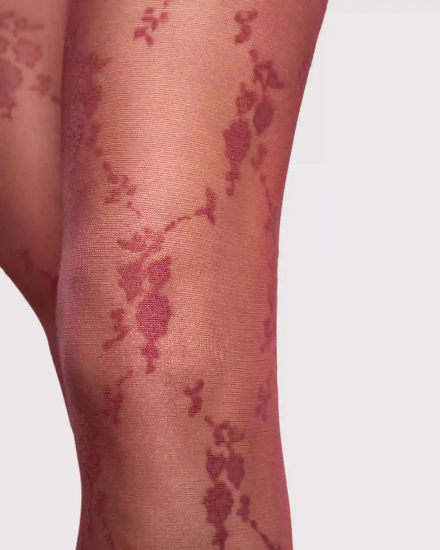 Close-up of sheer red hosiery on a leg featuring a dark red floral vine pattern over a warm nude base.