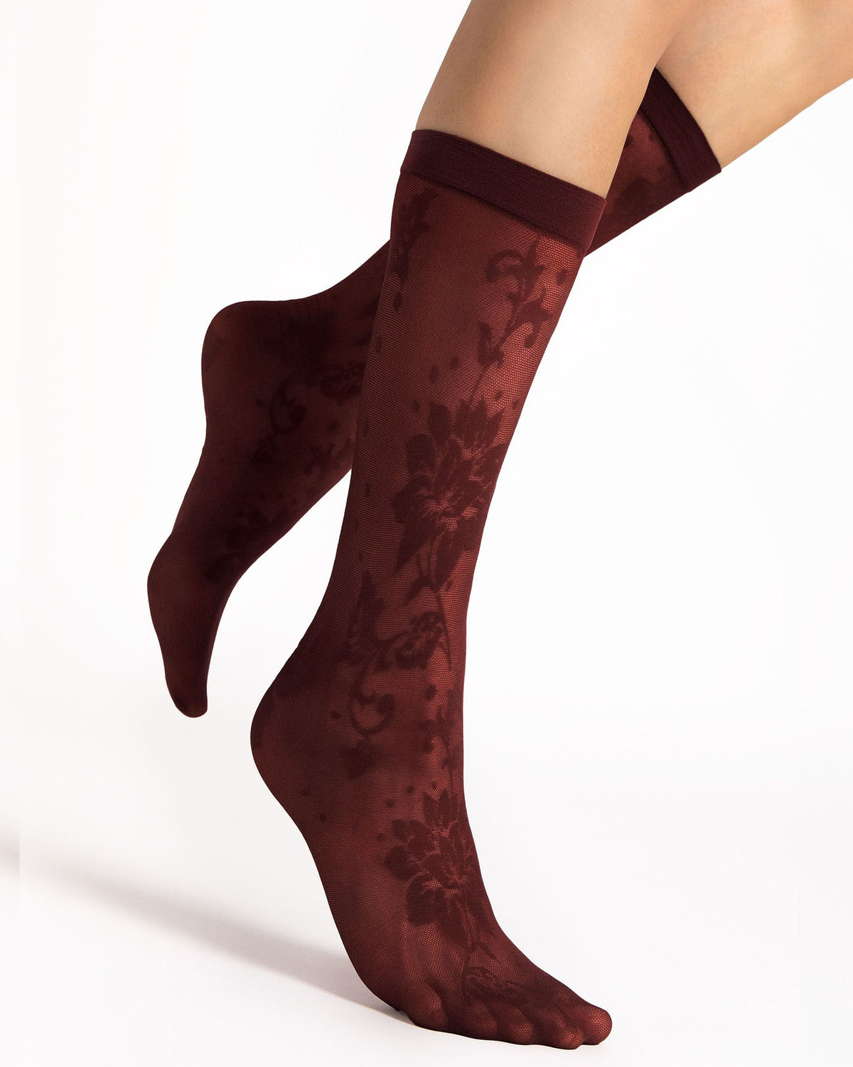 A pair of sheer knee-high socks with a dark floral damask pattern, shown on a model's feet against a clean white background.