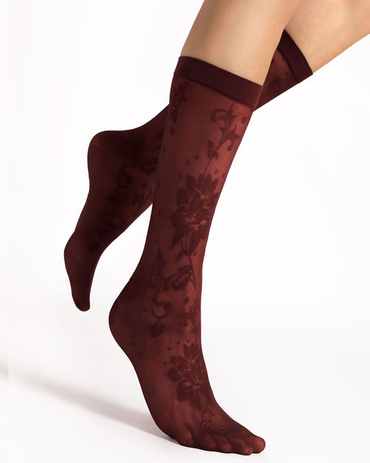 A pair of sheer knee-high socks with a dark floral damask pattern, shown on a model's feet against a clean white background.