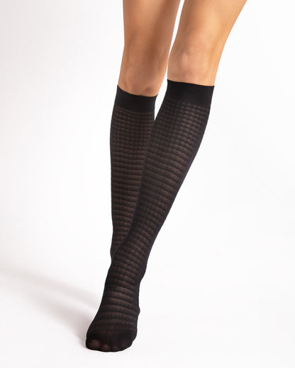 Black opaque patterned knee-high socks worn by a person on a white background