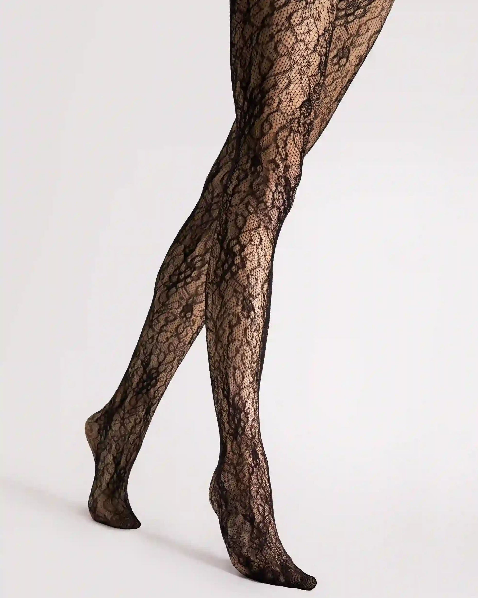 Black lace tights worn on a model's legs, shown from the thigh down against a plain light gray studio background.