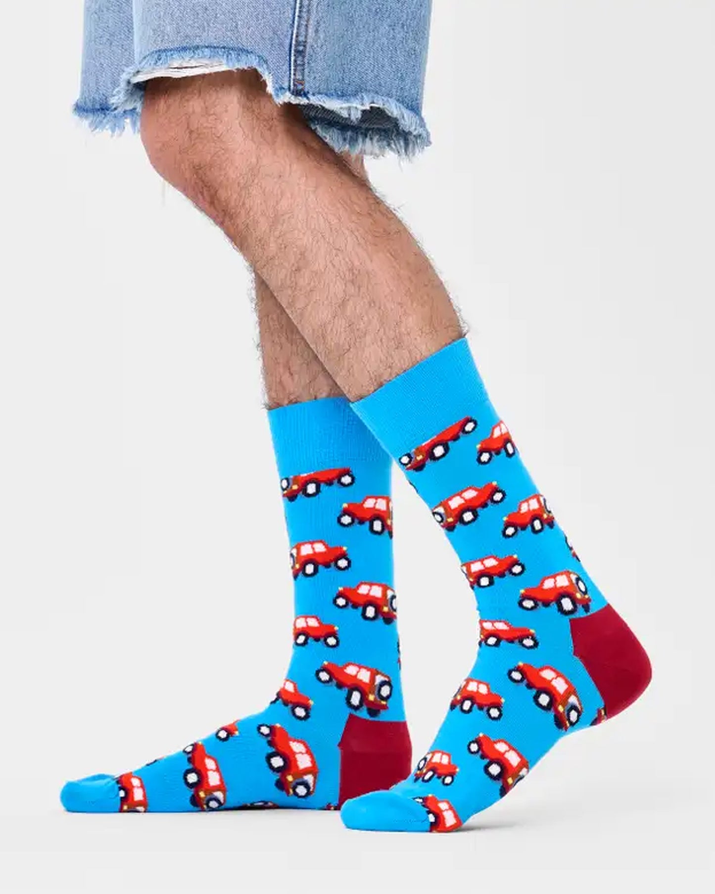 Happy Socks SUV Sock - Light blue crew cotton socks with an all over SUV type car pattern in shades of red and cream, worn by a man wearing cut off denim shorts