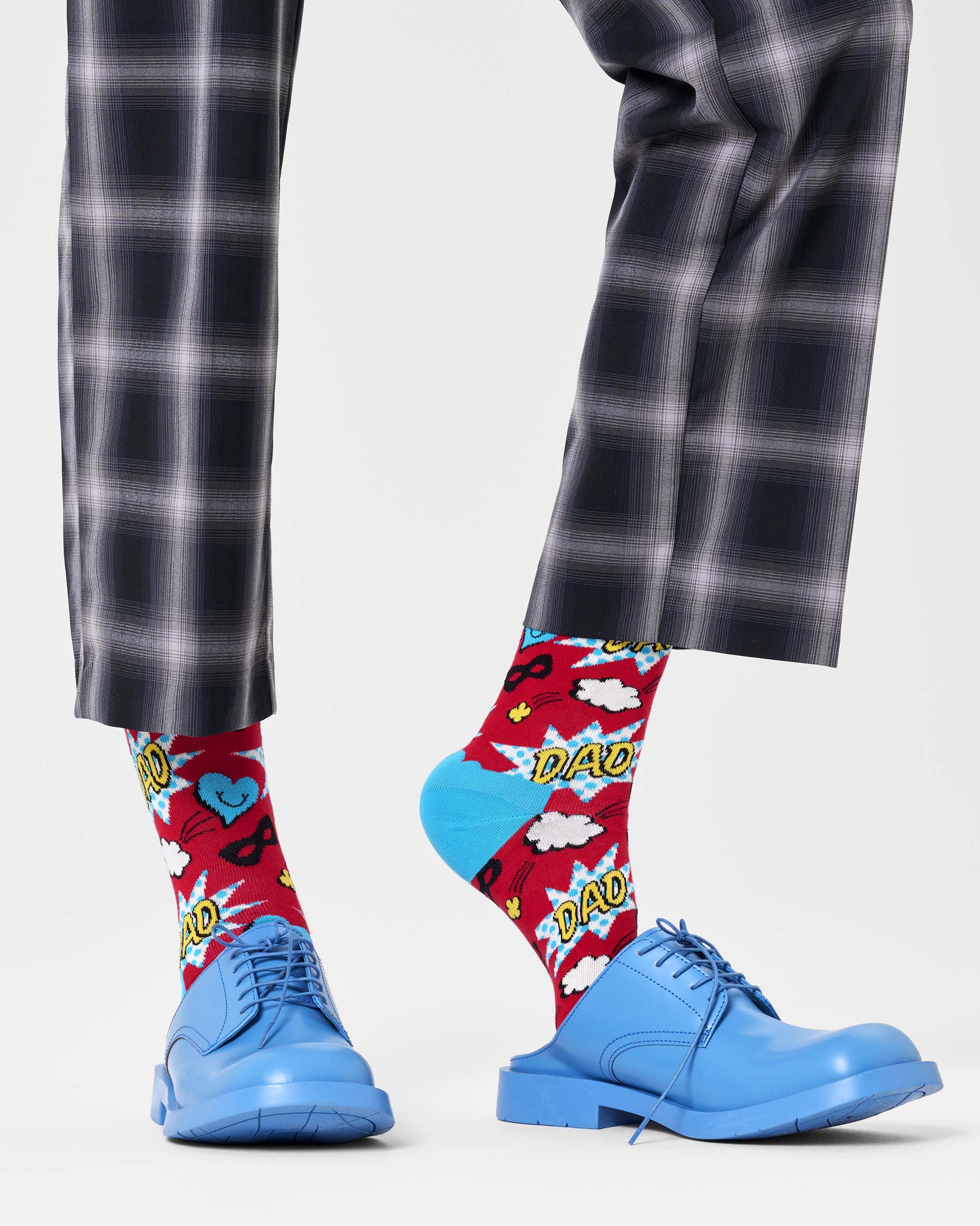 Person wearing red socks with comic-style designs and blue shoes on a light gray background