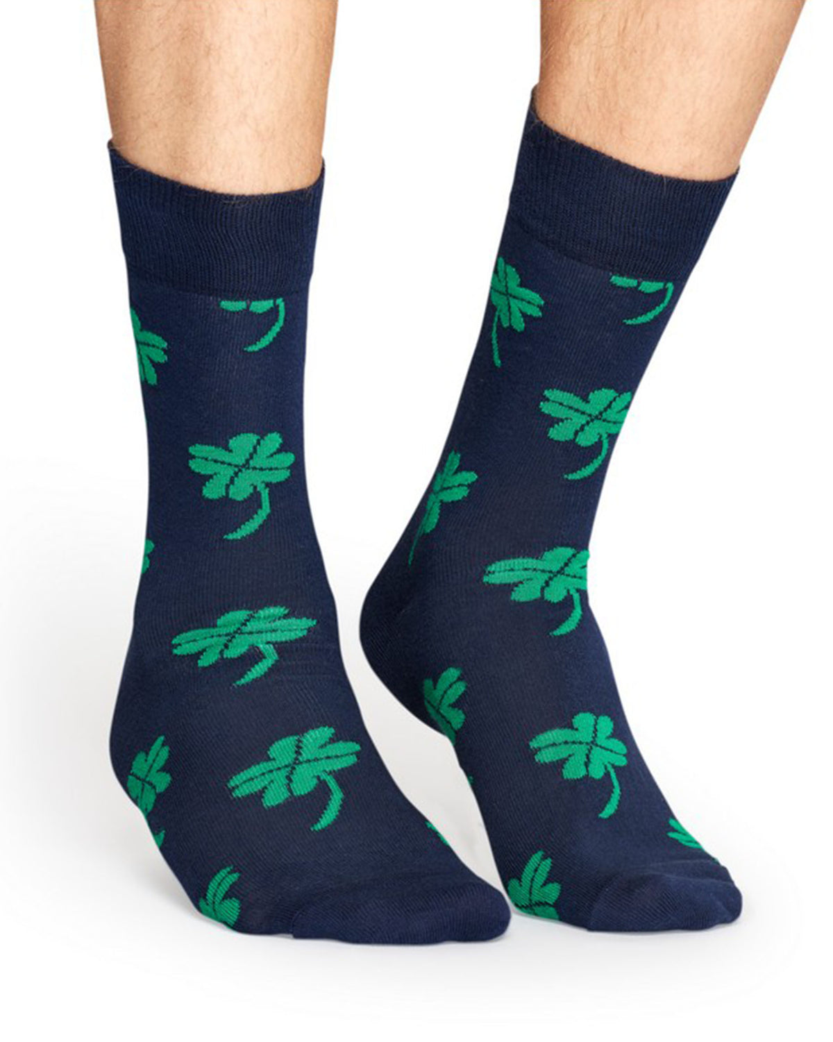A pair of navy blue crew socks with a green shamrock pattern, worn on a person's feet against a plain white background.