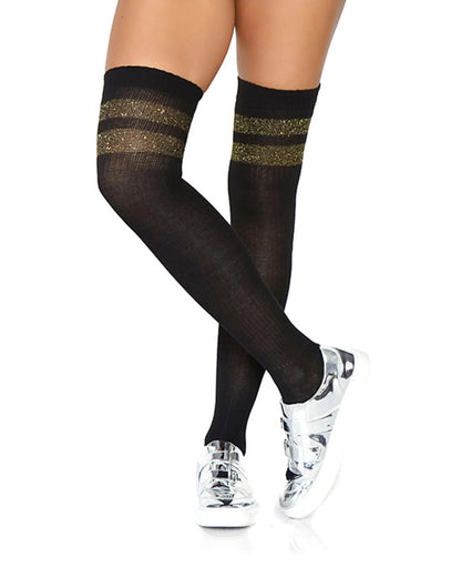 Black thigh-high socks with two horizontal glittery gold stripes near the top, shown on a model's legs paired with shiny gold sneakers against a white background.