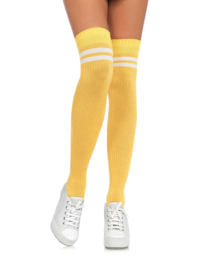 A person's legs wearing bright yellow ribbed over-the-knee socks with two white stripes near the top, paired with white sneakers, on a solid white background.