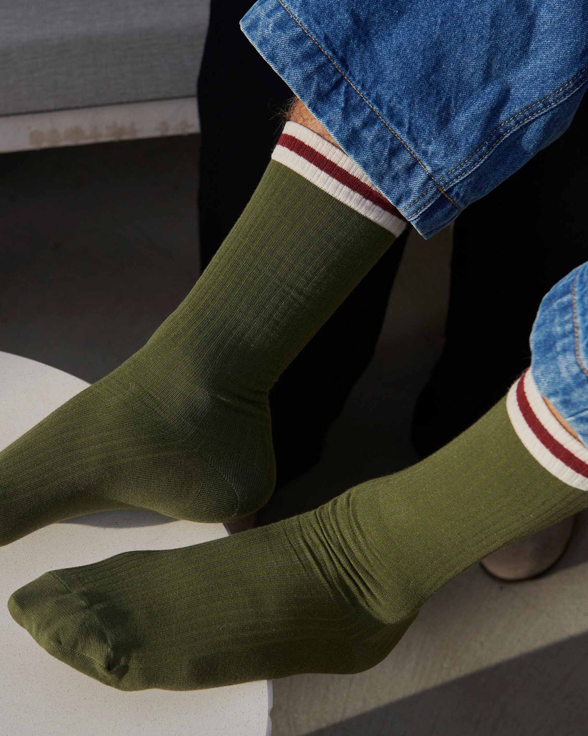 man wearing denim blue jeans and olive ribbed crew length socks with cream and wine sports stripe cuff.