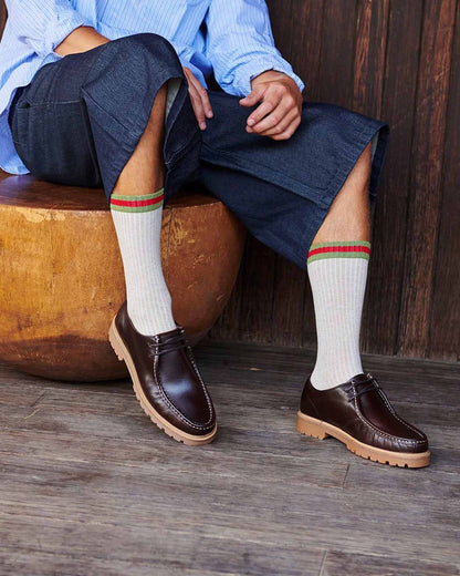 Man wearing cropped denim jeans and oat ribbed crew length socks with khaki green and red sports stripe cuff.