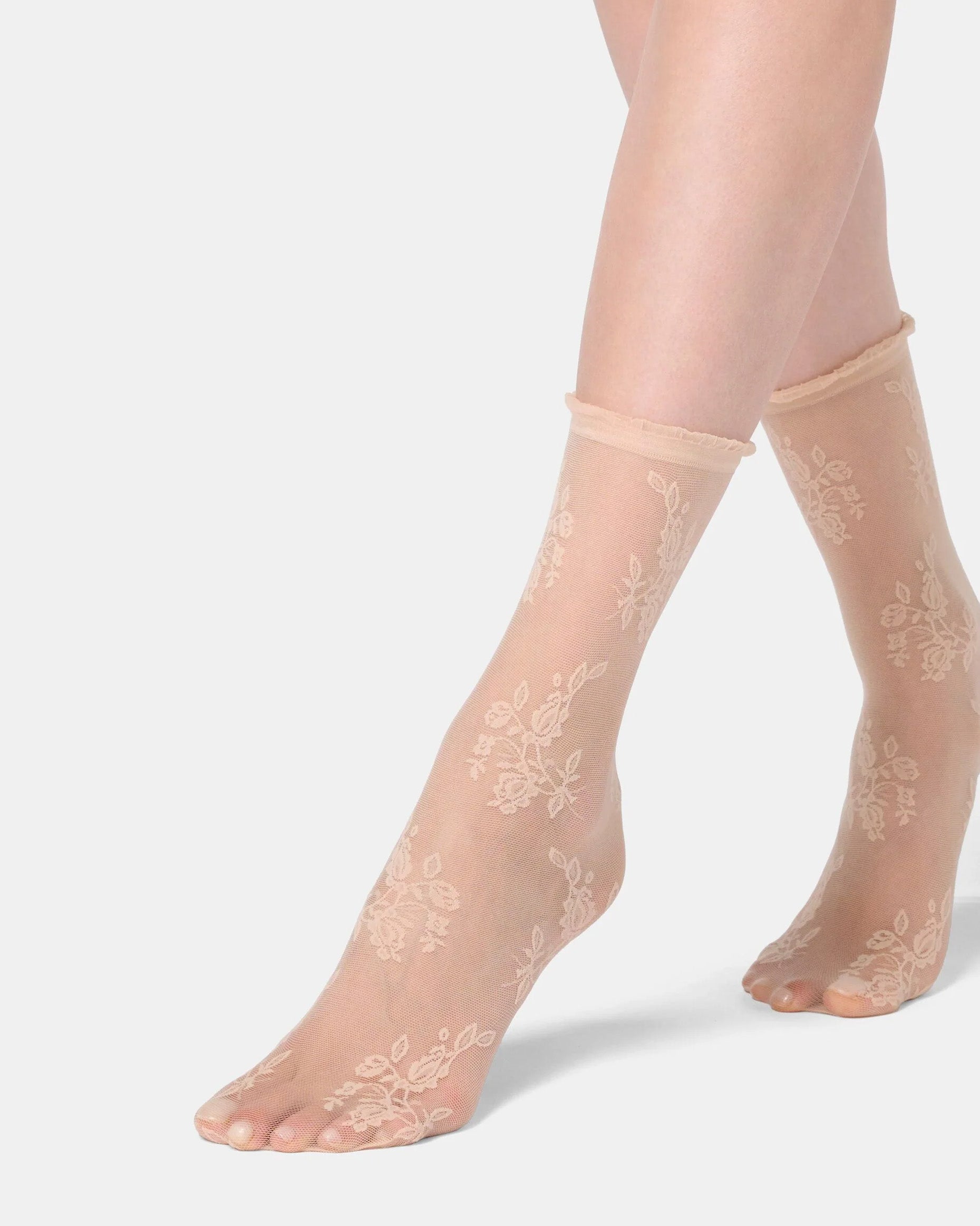 Sheer beige socks with floral lace design worn by a person on a light gray background