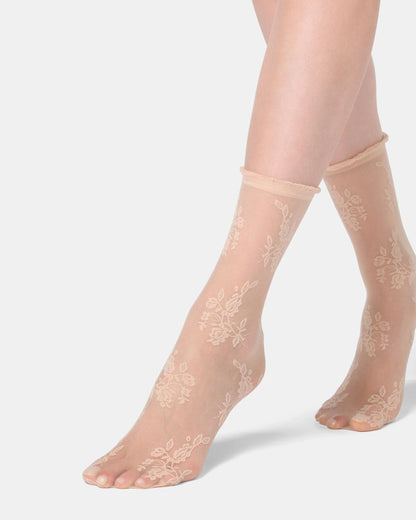 Sheer beige socks with floral lace design worn by a person on a light gray background
