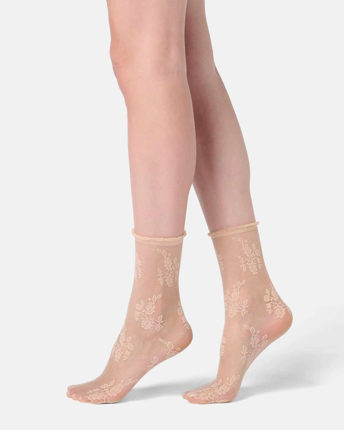 Sheer beige socks with floral lace design worn by a person on a light gray background