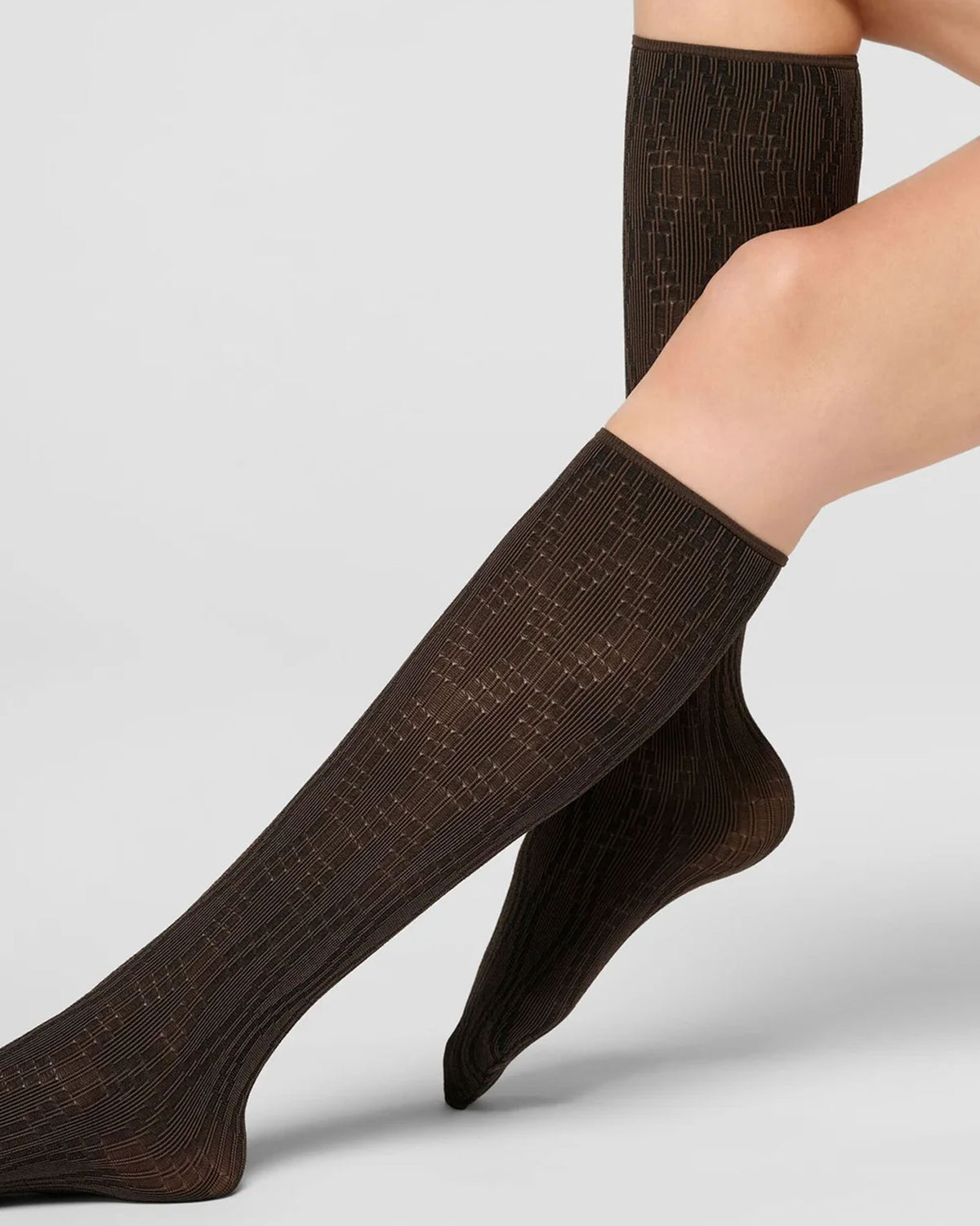 A pair of dark brown ribbed knee-high socks worn on a model's legs, shown against a light gray studio background.