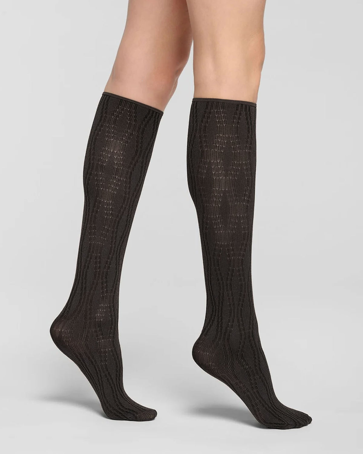 A pair of black knee-high ribbed socks worn on a model's legs, shown against a light gray studio background.