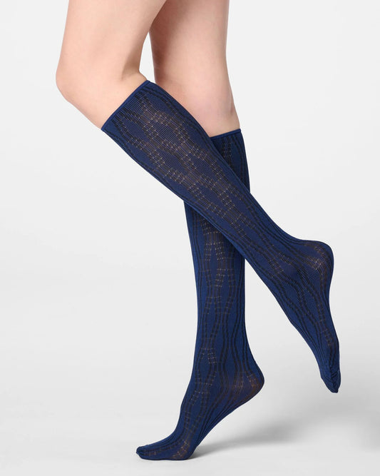 A pair of navy blue knee-high socks with a textured openwork knit pattern, shown on a model's legs against a light gray studio background.