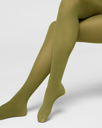 A close-up of a person's legs wearing solid olive green tights against a clean light gray studio background.