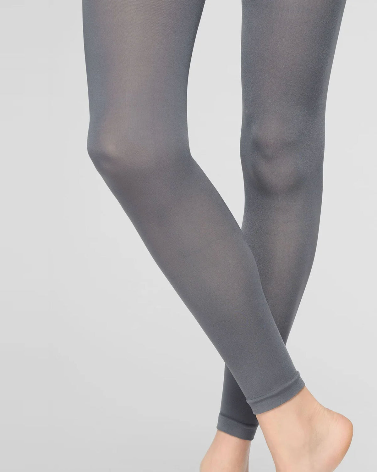A close-up of a person's legs wearing solid gray full-length footless tights against a light gray studio background.