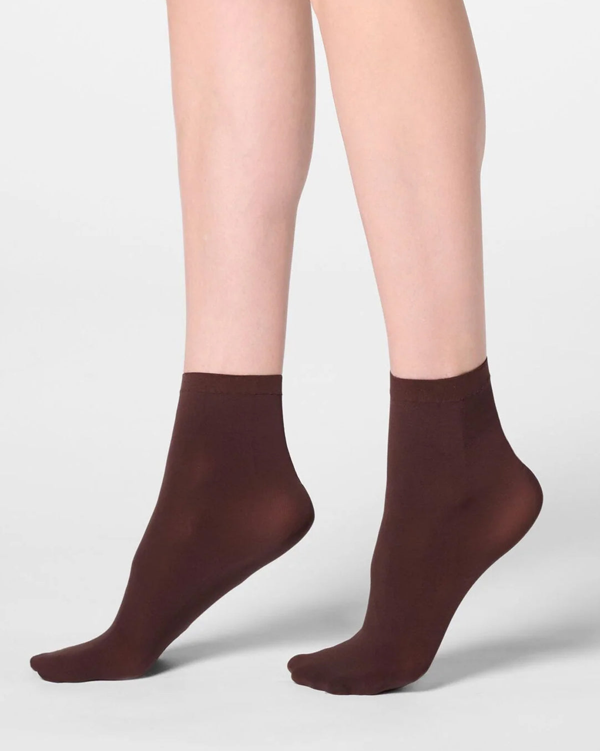 A pair of dark brown ankle socks worn on a model's feet, shown against a clean light gray studio background.