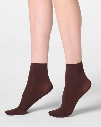 A pair of dark brown ankle socks worn on a model's feet, shown against a clean light gray studio background.