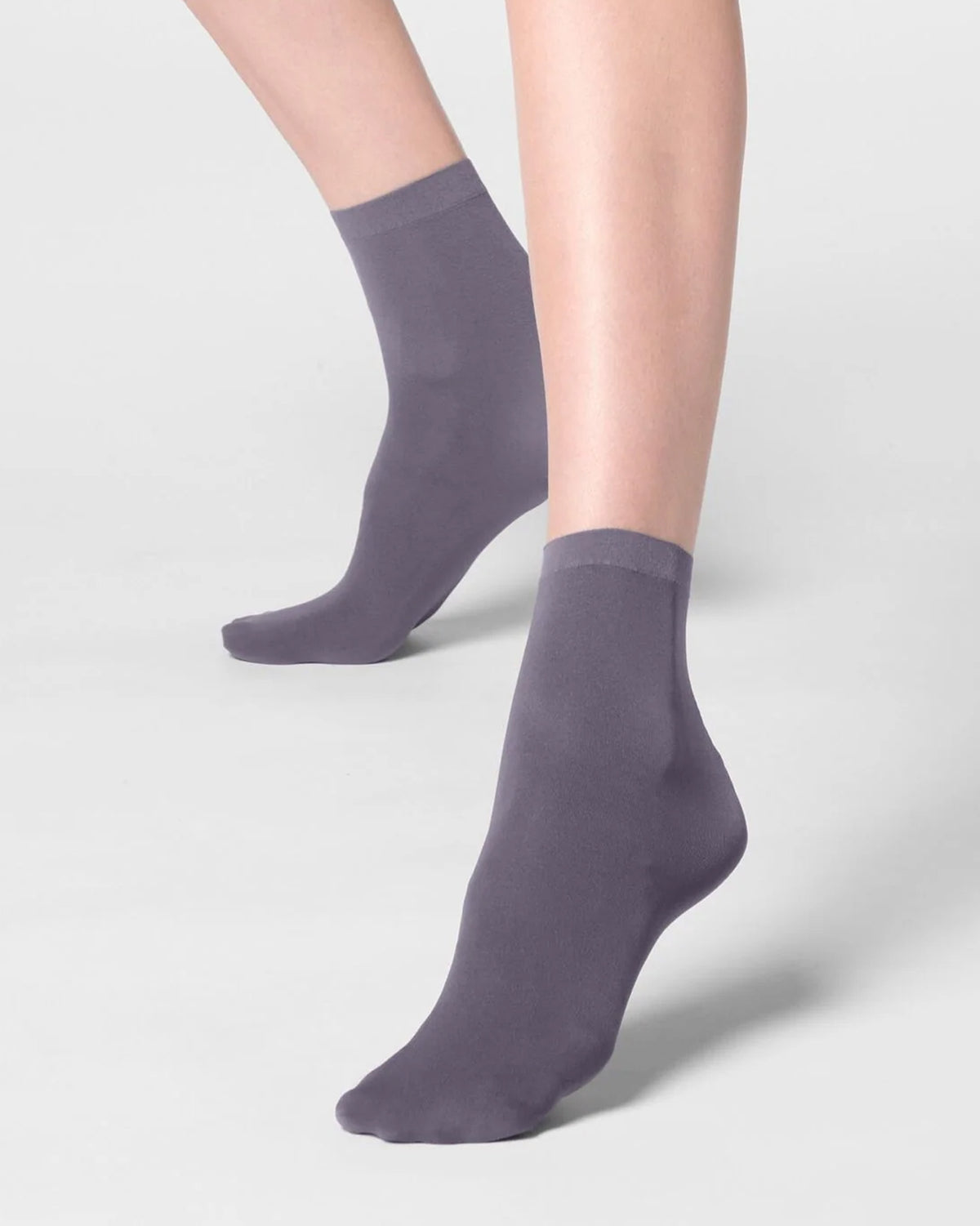 A pair of ankle-length socks in a muted dusty purple color, shown on a model's feet against a light gray studio background.