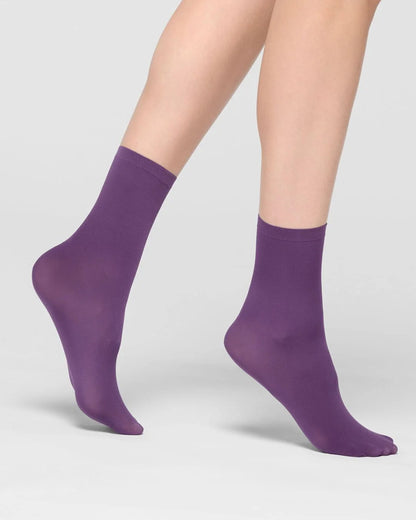 A pair of ankle-high socks in a solid purple color, shown on a model's feet against a light gray studio background.