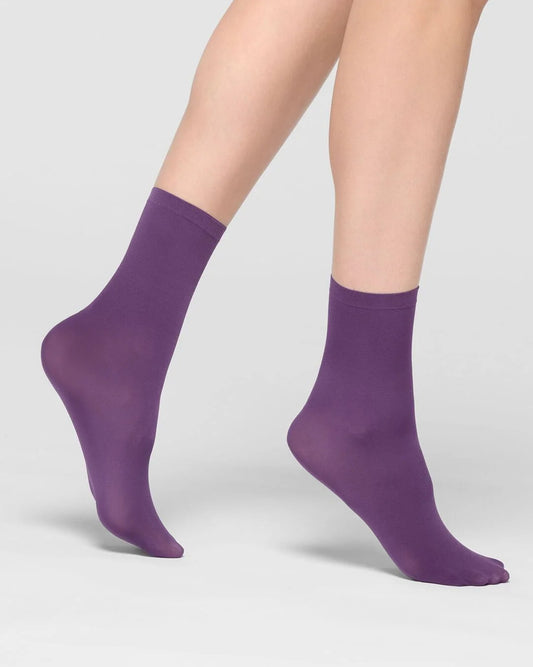 A pair of ankle-high socks in a solid purple color, shown on a model's feet against a light gray studio background.