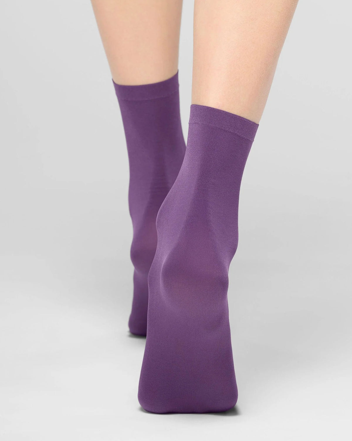 A pair of purple crew socks worn on a model's feet, shown against a clean light gray studio background.