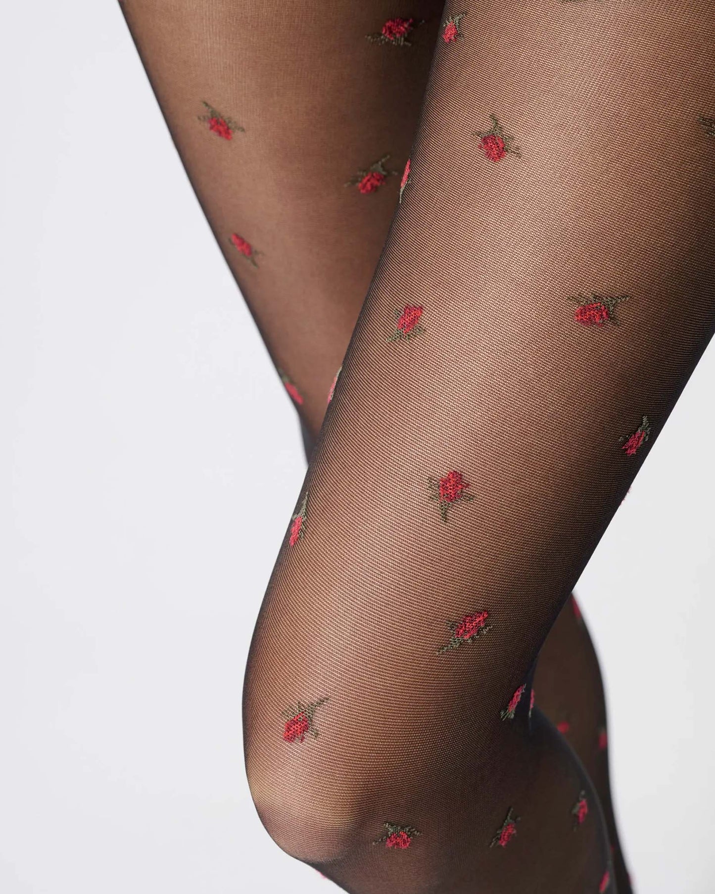 Sheer black fashion tights with red roses pattern, close up detail.