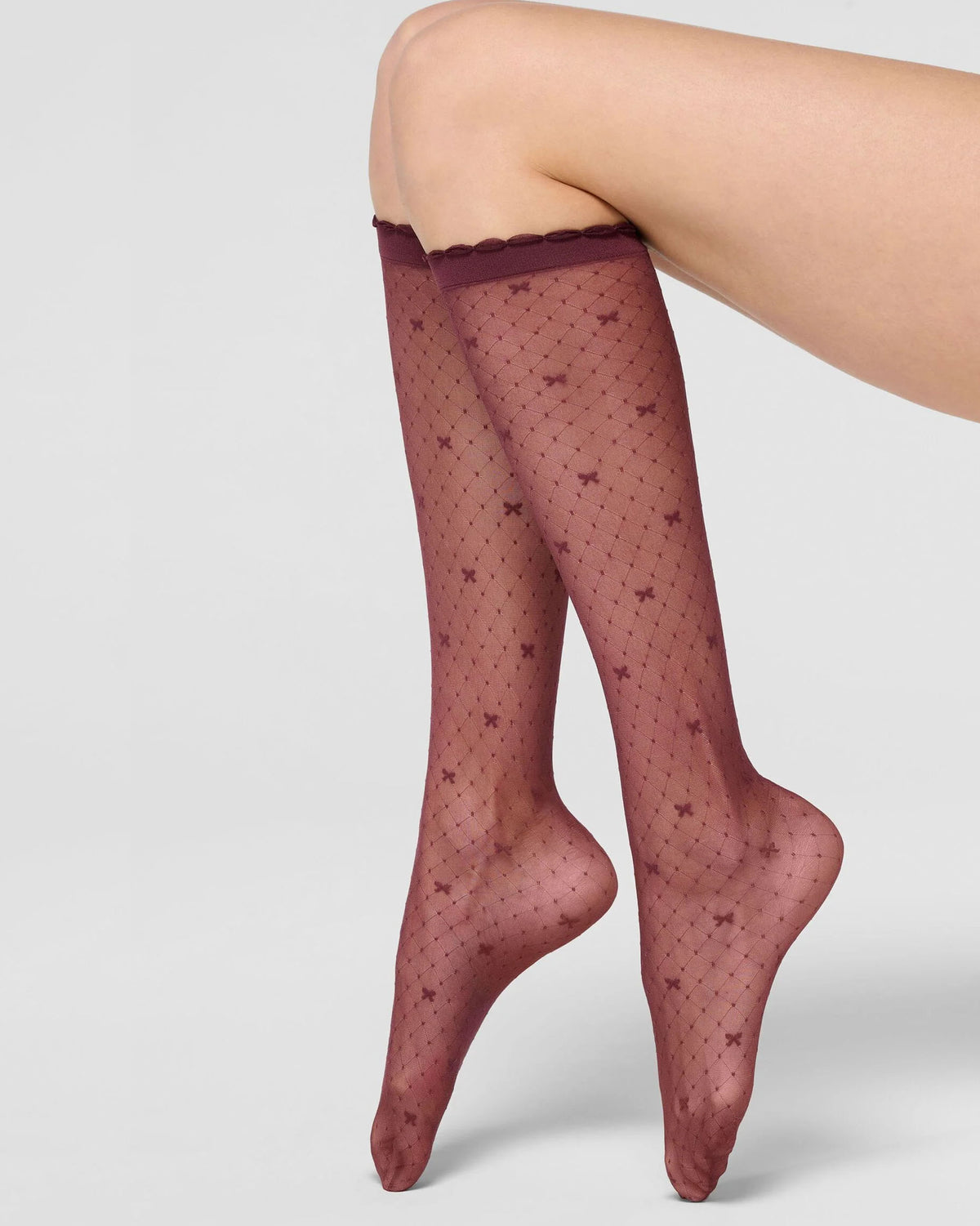 A pair of sheer knee-high stockings with a star pattern and scalloped top edge, shown on a model's legs against a light gray studio background.