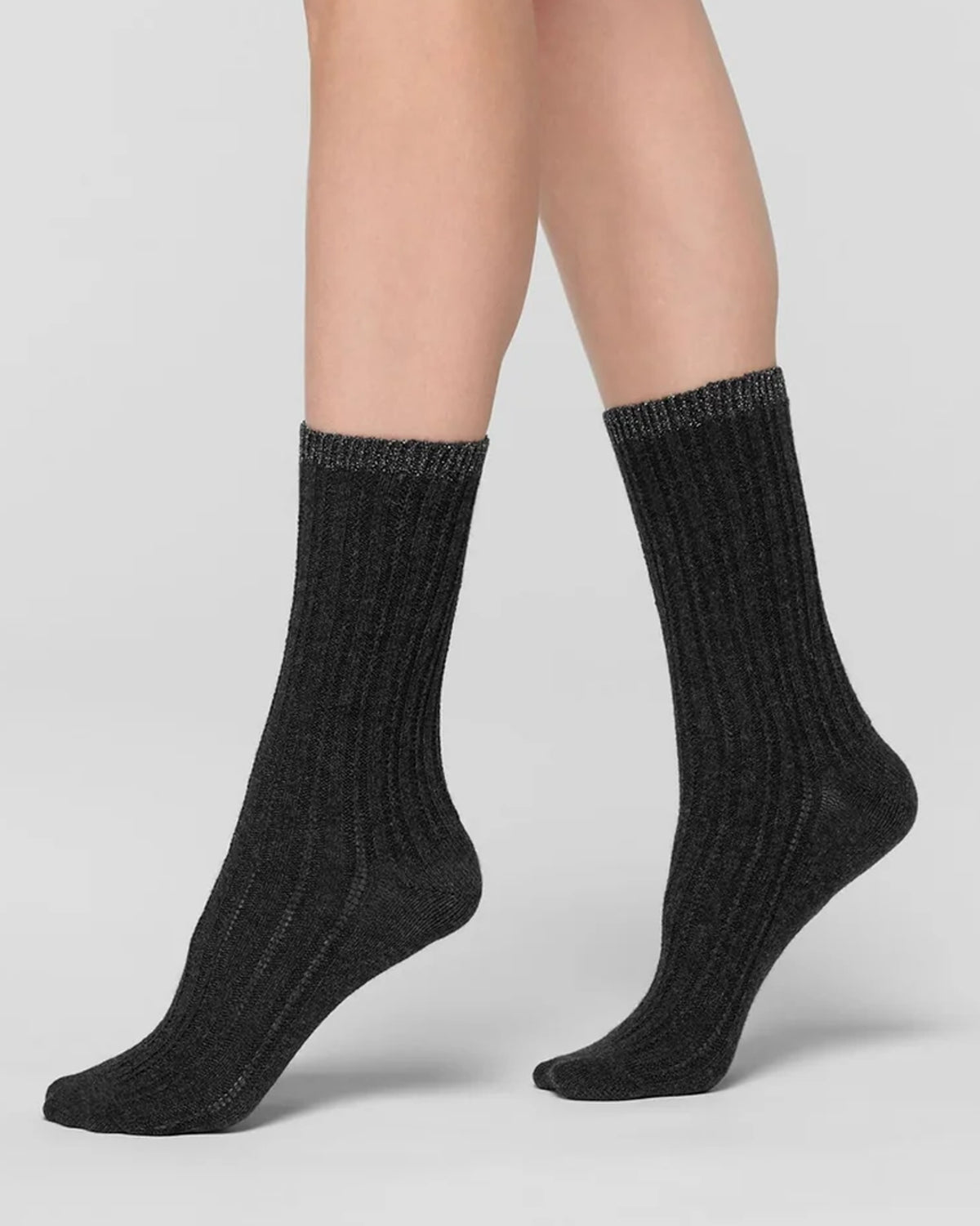 A pair of black ribbed knit thermal socks with lamé cuff worn on a model's feet, shown against a neutral light grey studio background.