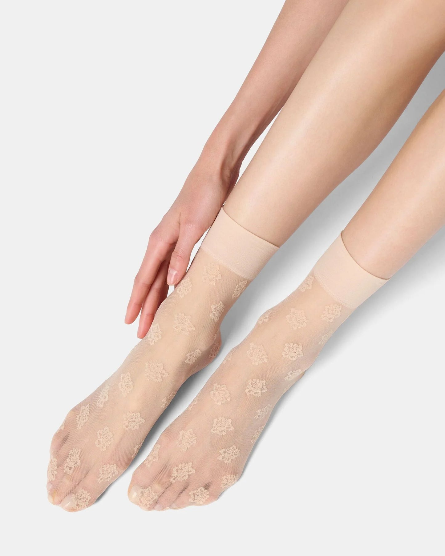 Beige sheer socks worn by a person on a light gray background